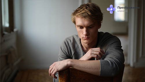 Мужчина сидит на полу и смотрит грустно вниз