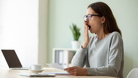 Девушка зевает сидя за столом на работе